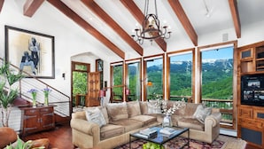 Ein geräumiges Wohnzimmer mit einer großen Eckcouch, einem Couchtisch und Blick auf eine gebirgige Landschaft durch große Fenster.