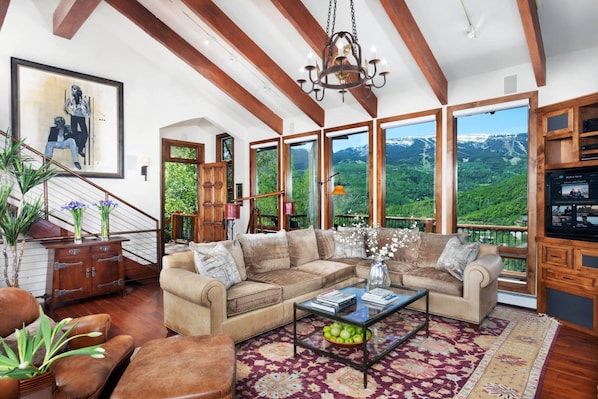A spacious living room with a large sectional sofa, a glass coffee table, and a view of a mountainous landscape through large windows.