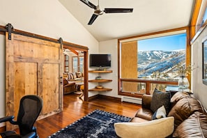 A spacious living room with a large window offering a mountain view, a ceiling fan, and a sliding barn door.