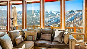 Ein gemütliches Zimmer mit einer großen Eckcouch, die auf eine malerische Berglandschaft durch große Fenster blickt.