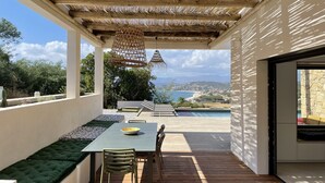 Une terrasse extérieure couverte, avec une table et des chaises, une piscine et une vue sur la mer.