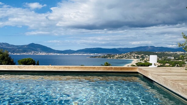 Une piscine aux eaux cristallines, offrant une vue sur une ville côtière et des montagnes en arrière-plan.