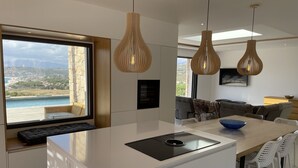 Une cuisine moderne dotée d’un grand îlot central, d’un four encastré et offrant une vue sur la mer.