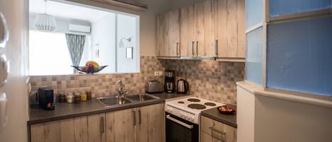 A compact kitchen with wooden cabinets, a gas stove, a sink, and a window with a view of the outdoors.