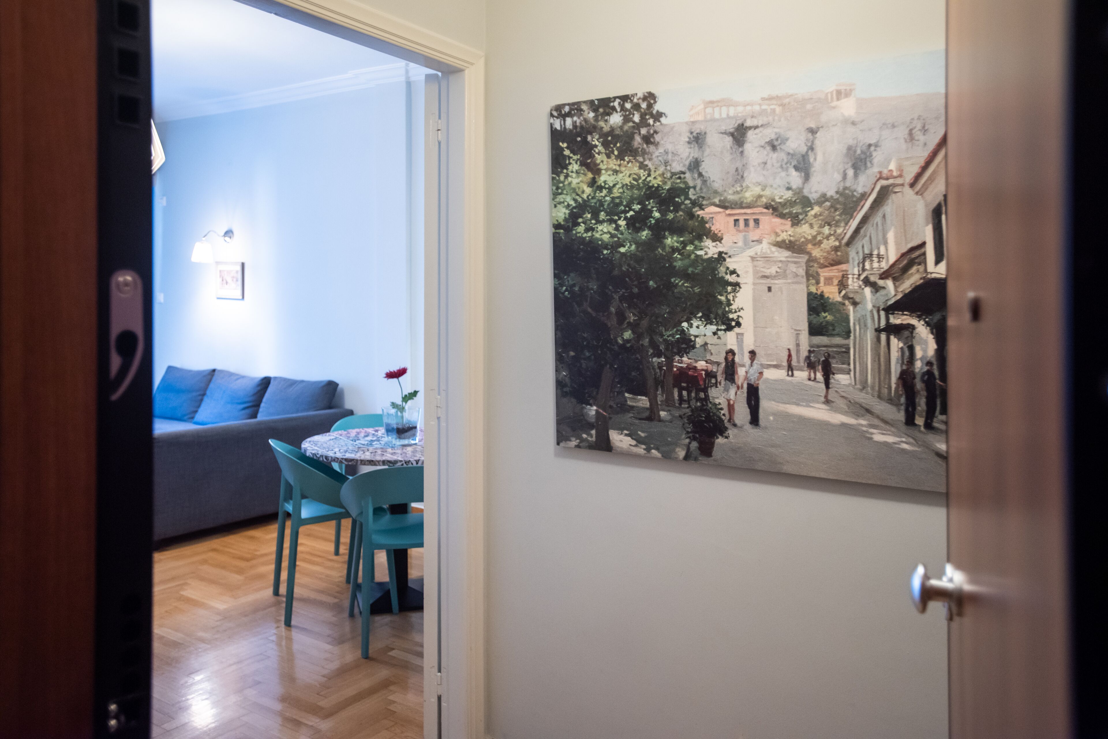 Ein Zimmer mit Essbereich, ausgestattet mit einem Tisch, Stühlen, einer Couch und einem an der Wand hängenden Bild von einer Straßenszene.