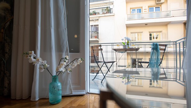 Un balcón con una mesa, sillas y un florero con flores.