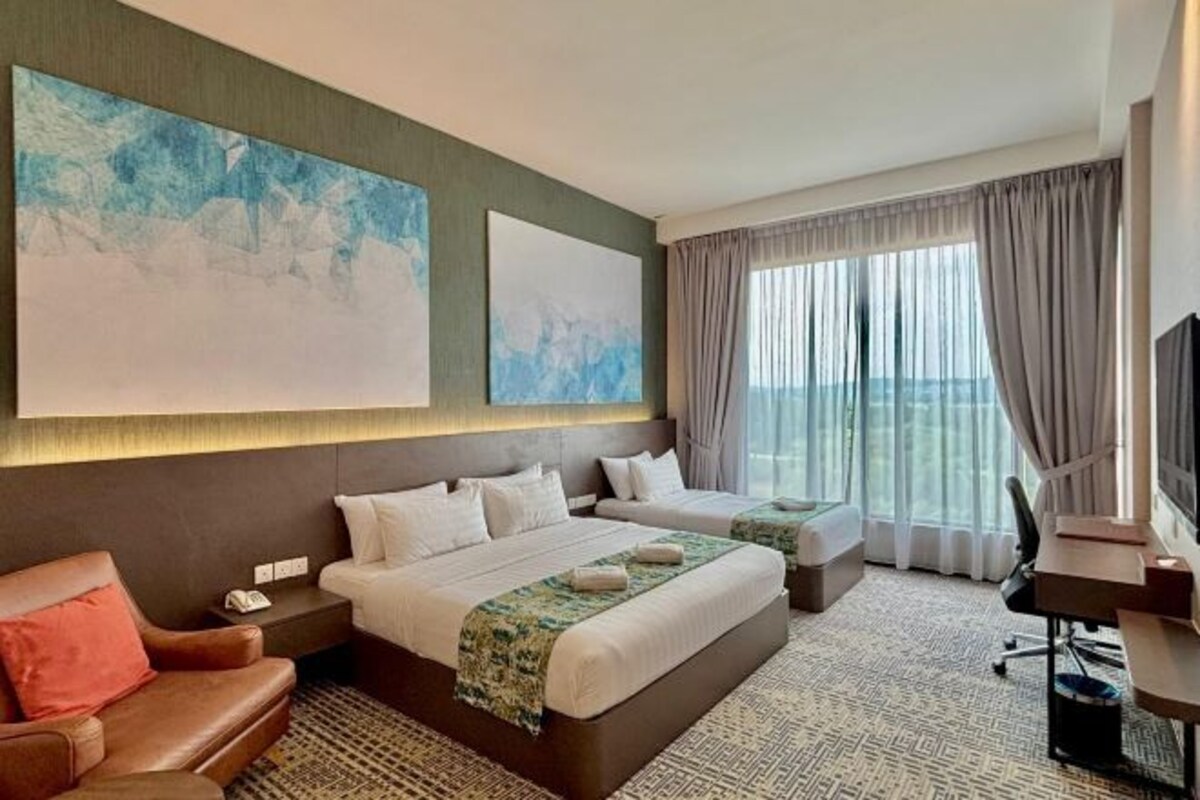 Une chambre d’hôtel avec deux lits, un bureau, une chaise et de grandes fenêtres avec des rideaux.