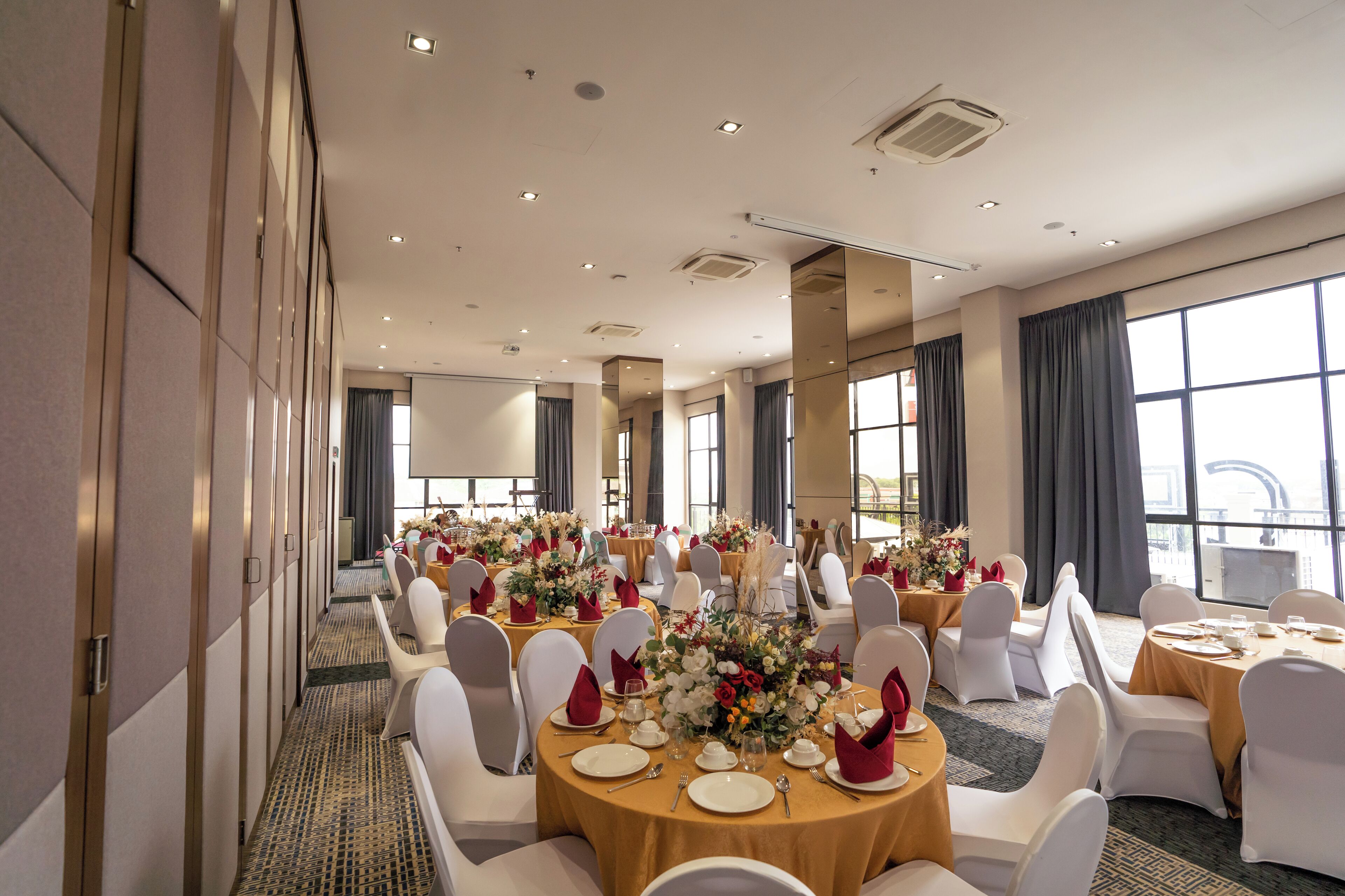 Un salón de conferencias con mesas redondas, sillas blancas y centros de mesa florales.