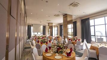 Un salón de conferencias con mesas redondas, sillas blancas y centros de mesa florales.