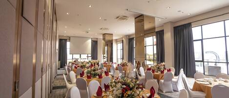 Un salón de conferencias con mesas redondas, sillas blancas y centros de mesa florales.