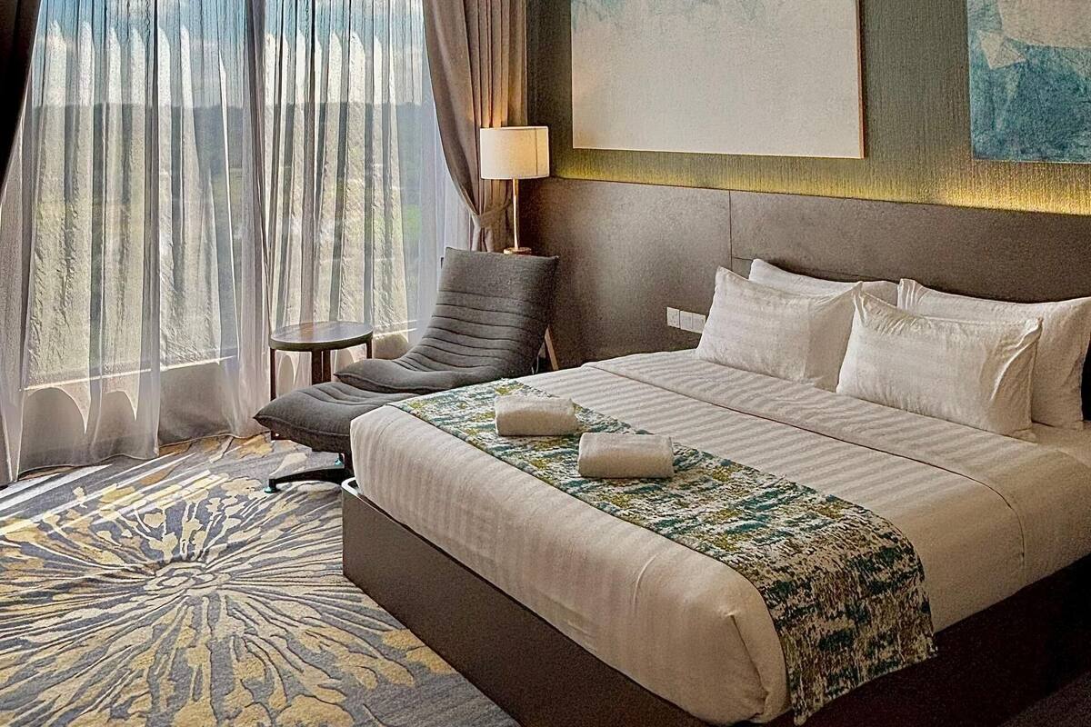 Una habitación de hotel con una cama grande, una silla, un escritorio y un ventanal con cortinas.