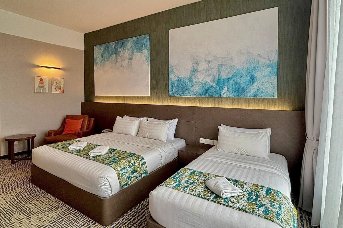 Una habitación de hotel con dos camas, un sofá, una mesita y obras de arte en las paredes.