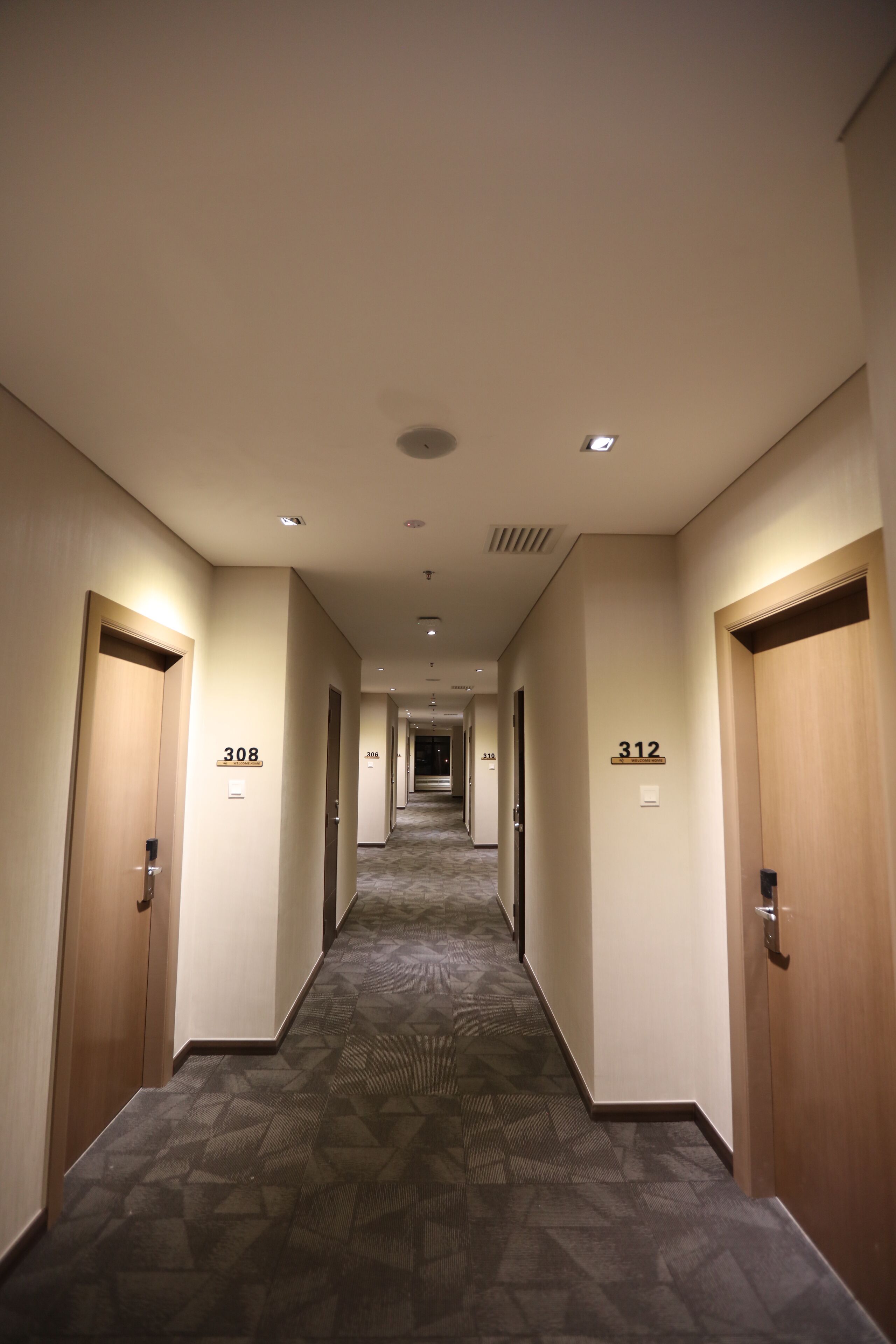 Pasillo de hotel con puertas numeradas 308 y 312, suelos alfombrados e iluminación empotrada.