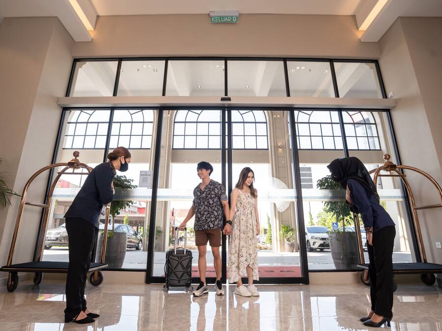 A hotel lobby with large windows, a reception desk, and a luggage cart.