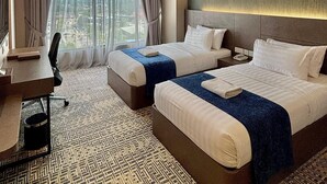 Quarto de hotel com duas camas, uma escrivaninha e uma janela grande com cortinas.