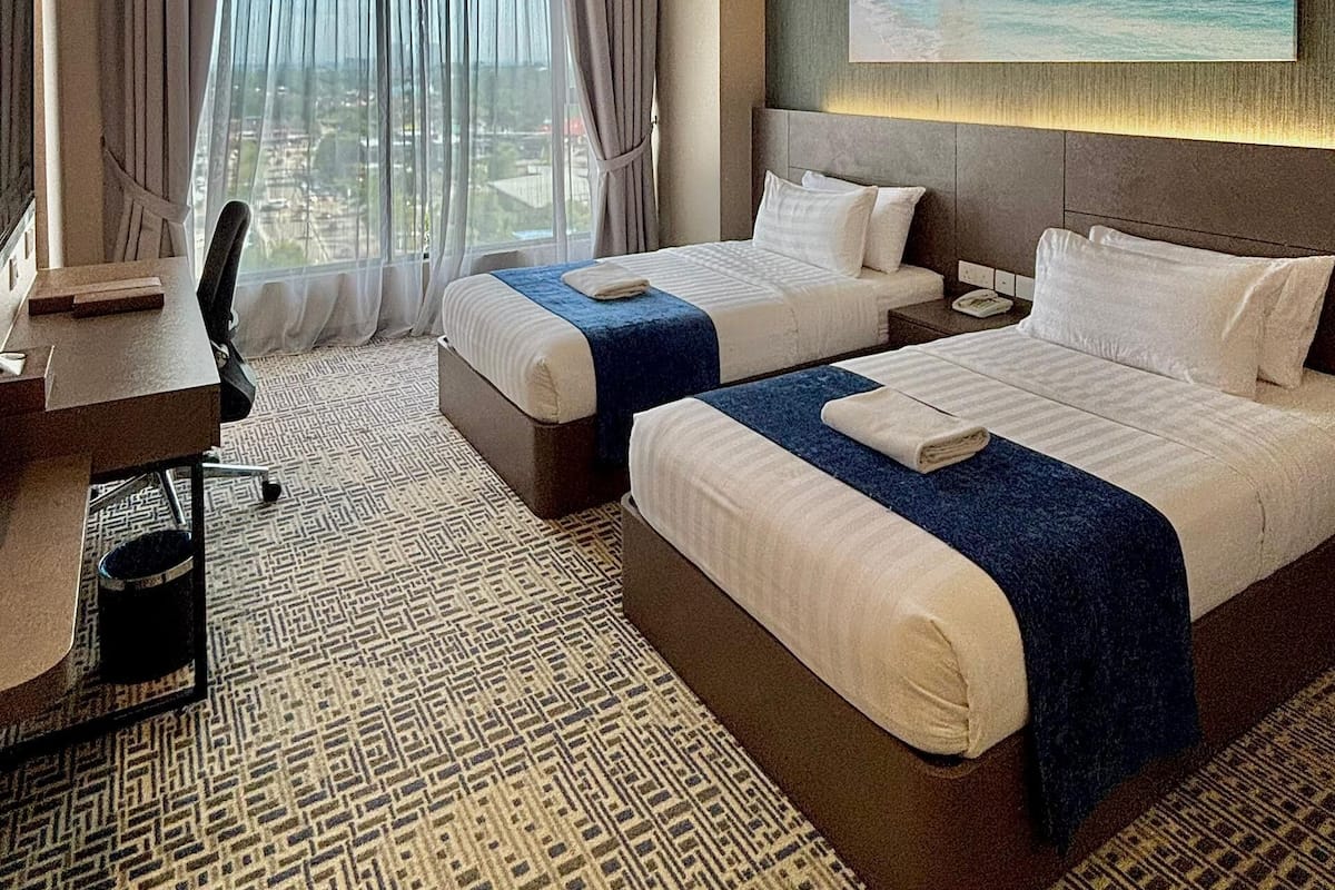 Una habitación de hotel con dos camas, un escritorio y un ventanal grande con cortinas.