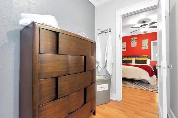 A bedroom with a wooden wardrobe, a grey laundry basket, and a bed with a red headboard. - Downtown Studio by Toyota Center/Minute Maid/ George R Brown (Houston)