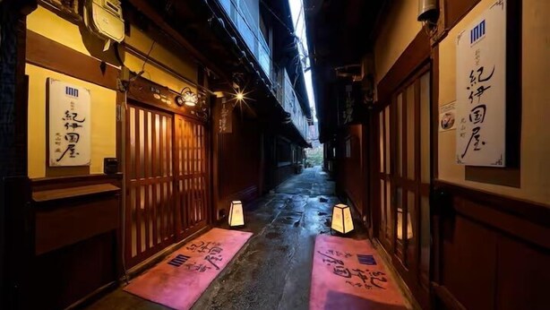 Un estrecho callejón con puertas de madera y señalización tradicional japonesa.