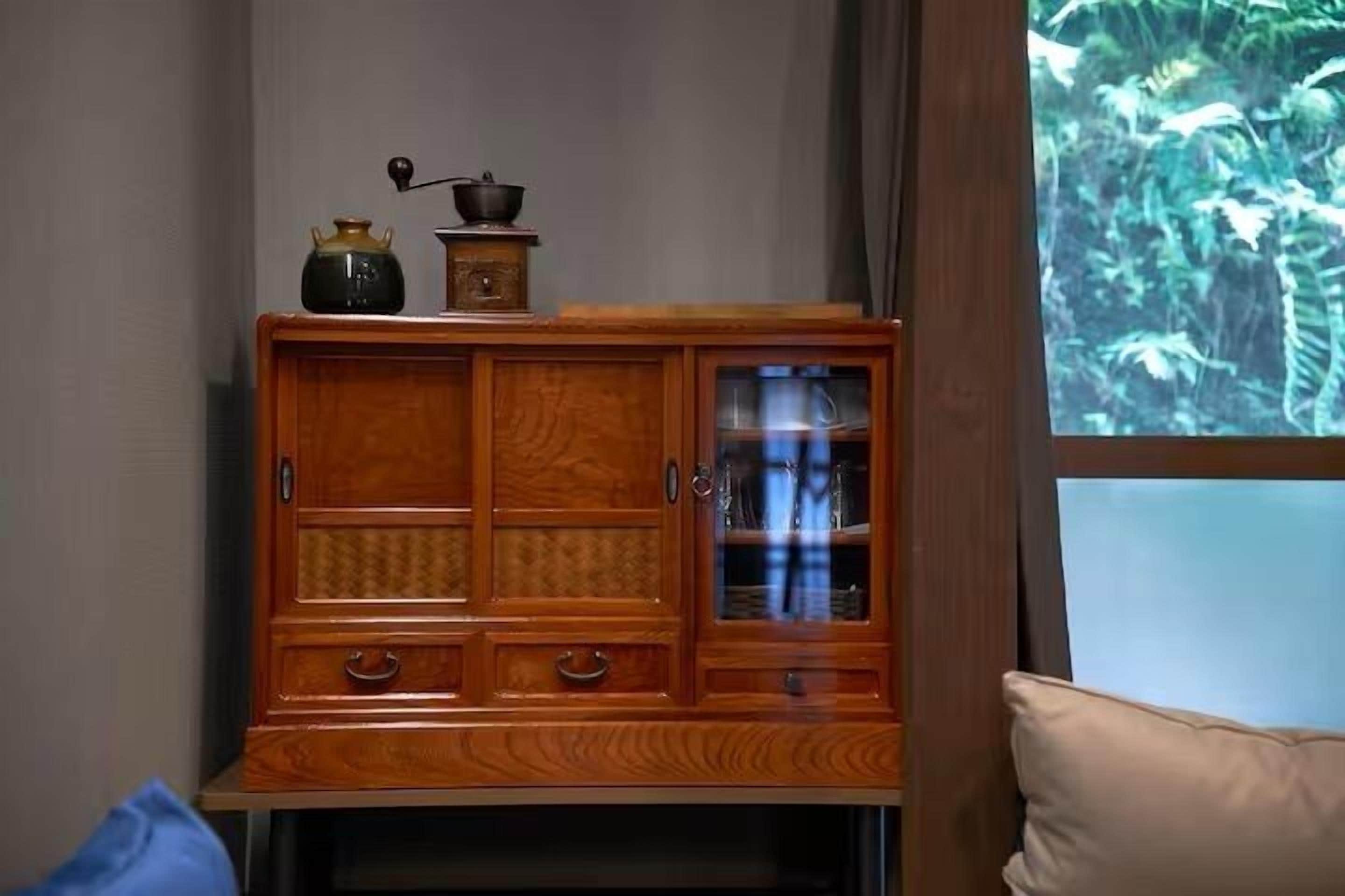 A wooden cabinet with glass doors and drawers, placed against a wall with a window showing a forest view.