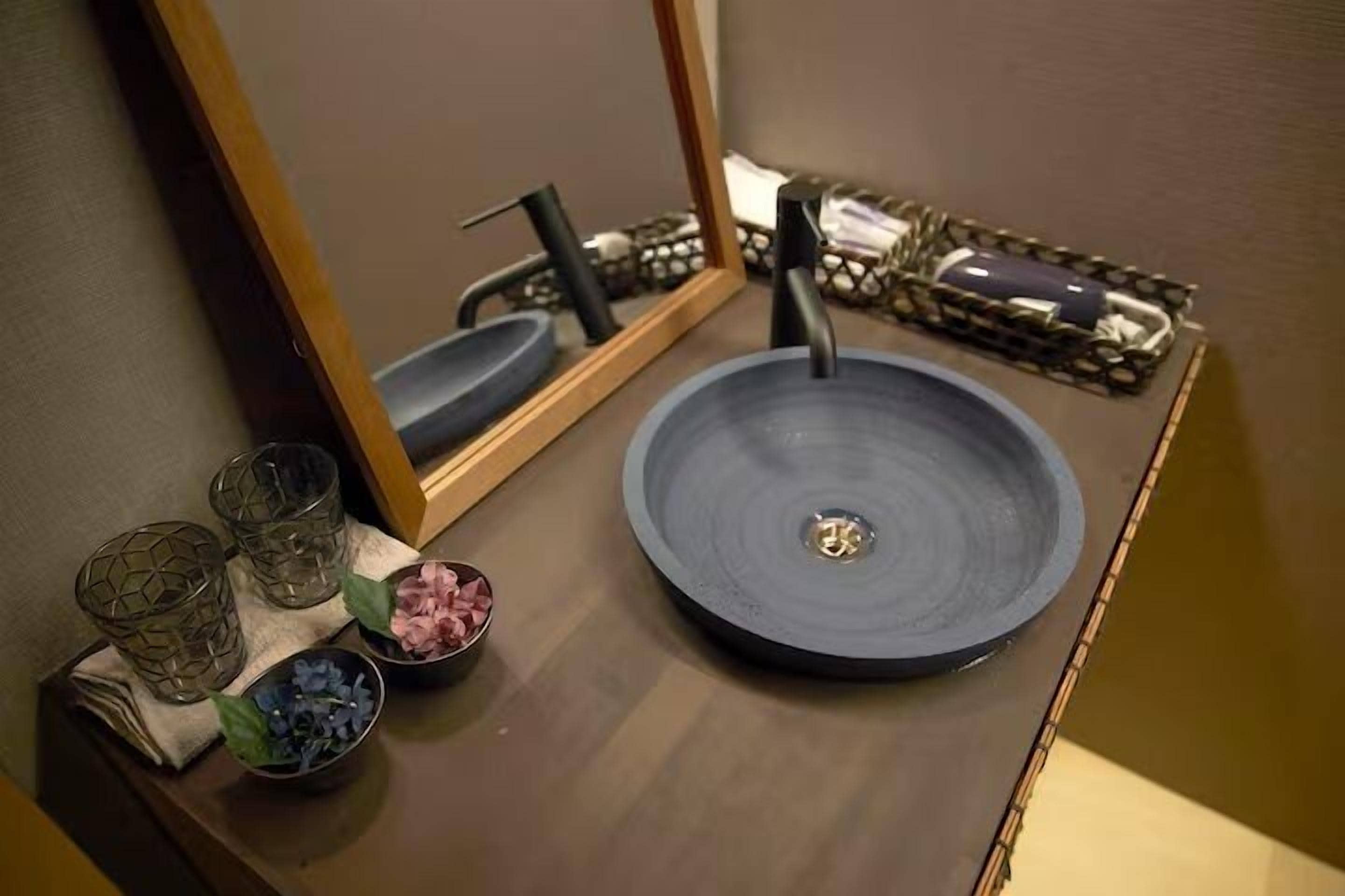 A bathroom with a round sink, a mirror, and decorative items including glass vases and bowls with flowers.