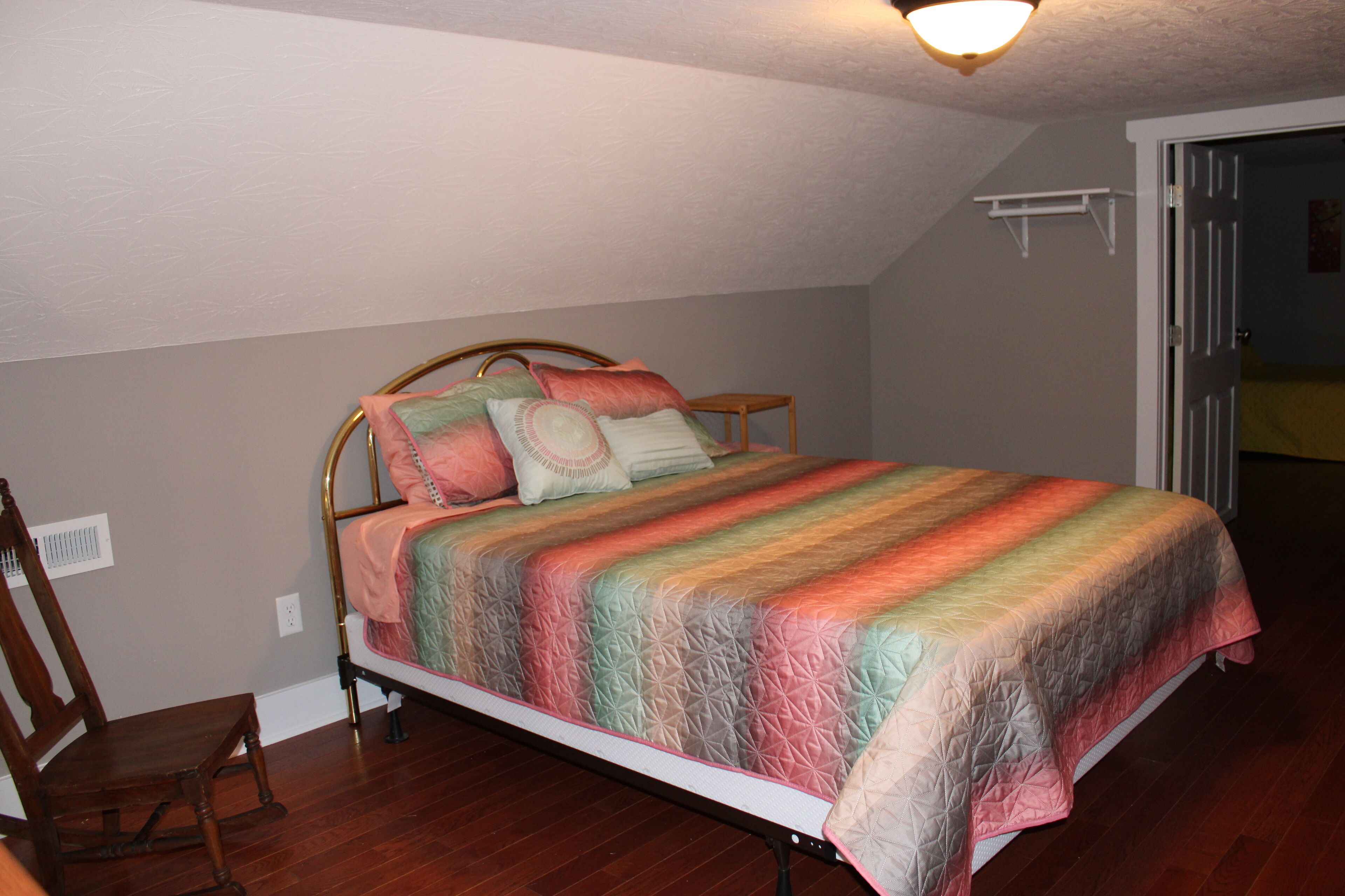 A bedroom with a bed, a wooden chair, and a door leading to another room.