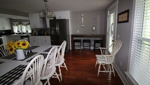 Een ruime keuken met witte kasten, een roestvrijstalen koelkast, en een eethoek met witte stoelen en een tafel voor vier personen.