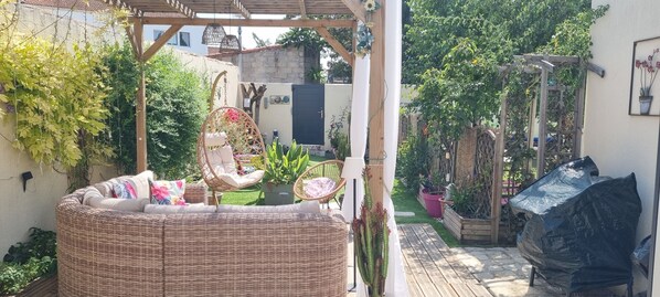 Un espacio de estar al aire libre techado, con mobiliario de mimbre y una silla colgante.