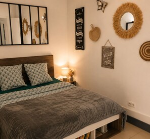 Een slaapkamer met een bed, kussens, een bedlampje, een spiegel aan de muur en decoratieve muurdecoratie.