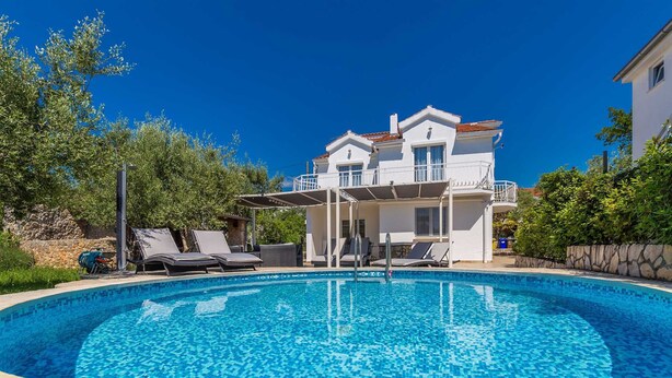 A two-story house with a swimming pool, outdoor seating, and a stone wall.
