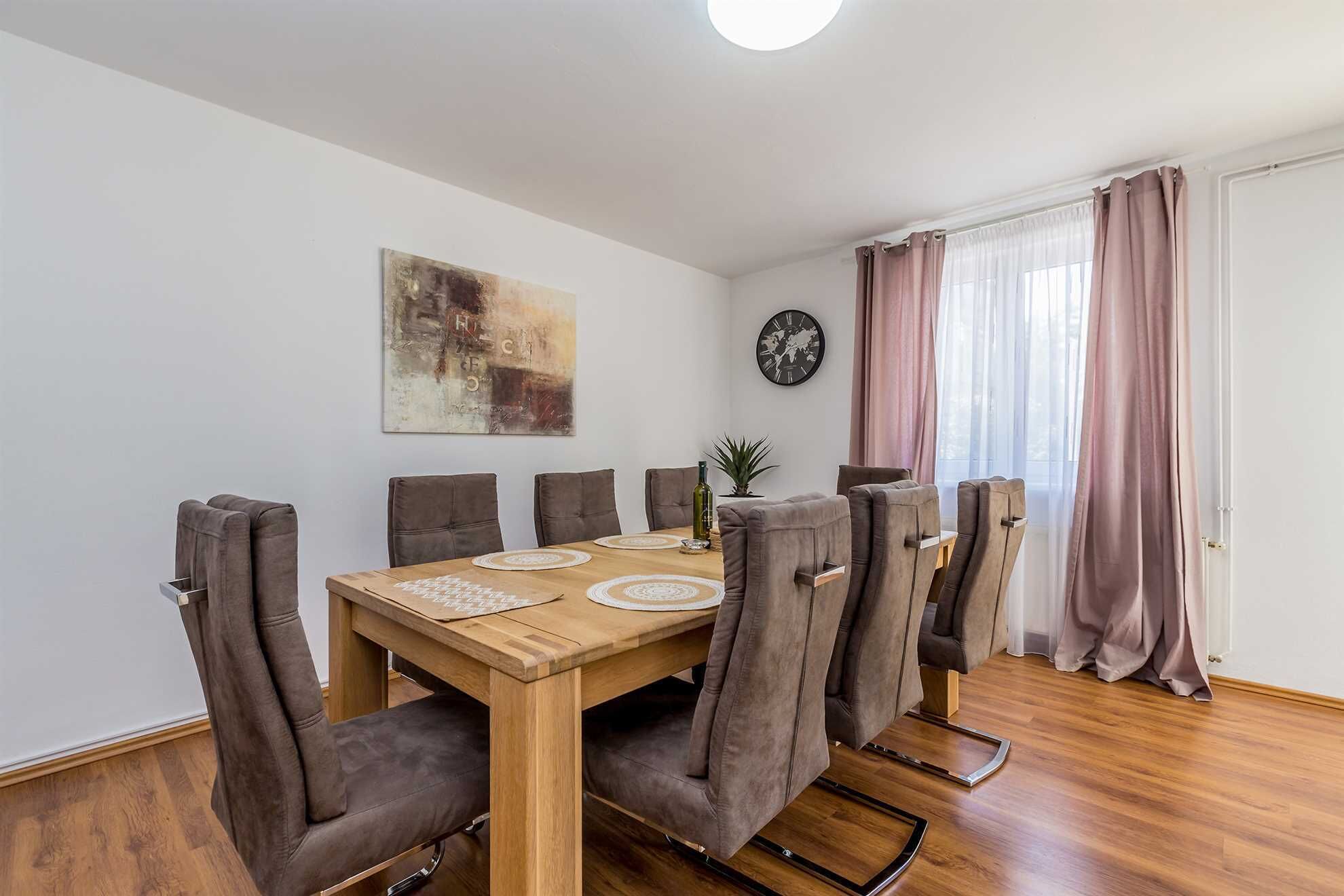 A dining area with a wooden table and six chairs, a world map on the wall, and a clock.