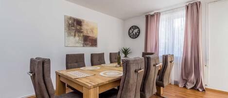A dining area with a wooden table and six chairs, a world map on the wall, and a clock.