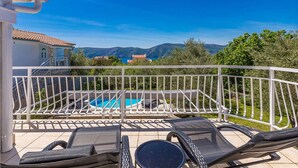 A balcony with a pool, outdoor seating, and a view of mountains.