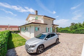 Ein zweistöckiges Haus mit Natursteinfassade, ein Auto davor und einem gepflegten Rasen.