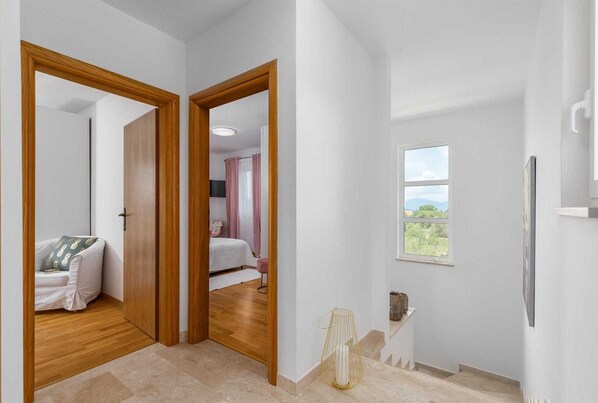 A hallway with wooden doors leading to a bedroom with a bed and a TV. There is a window with a view of greenery. - Holiday house JOSEPHINE with heated swimming pool (Linardići)