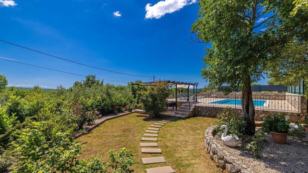 Ein Garten mit einem Kiesweg, einer Pergola, einem Swimmingpool und verschiedenen Pflanzen.