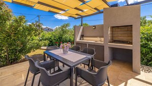 Eine Terrasse im Freien mit Grill, Sitzgelegenheiten und einem Tisch.