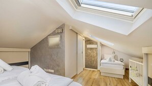 Ein Schlafzimmer mit Dachfenster, einem Bett, einem Nachttisch, einem kleinen Schreibtisch und einem Babybett.