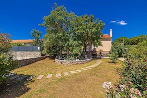 Un giardino con un vialetto in pietra, una fontana e un edificio con tetto in tegole.