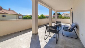 A covered outdoor area with a table and chairs, a view of neighboring buildings, and a clear sky.