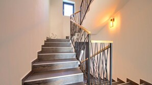A staircase with dark steps and a black metal railing, leading to a landing with a small window.