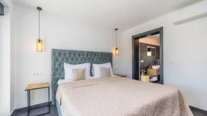 A modern bedroom with a tufted headboard, a quilted bedspread, bedside tables, and pendant lighting.