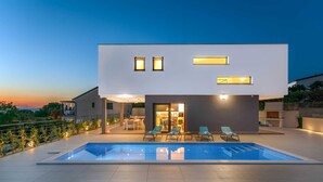 Une maison moderne à deux étages, dotée d’une piscine, d’un espace salon extérieur et offrant une vue sur le coucher de soleil.
