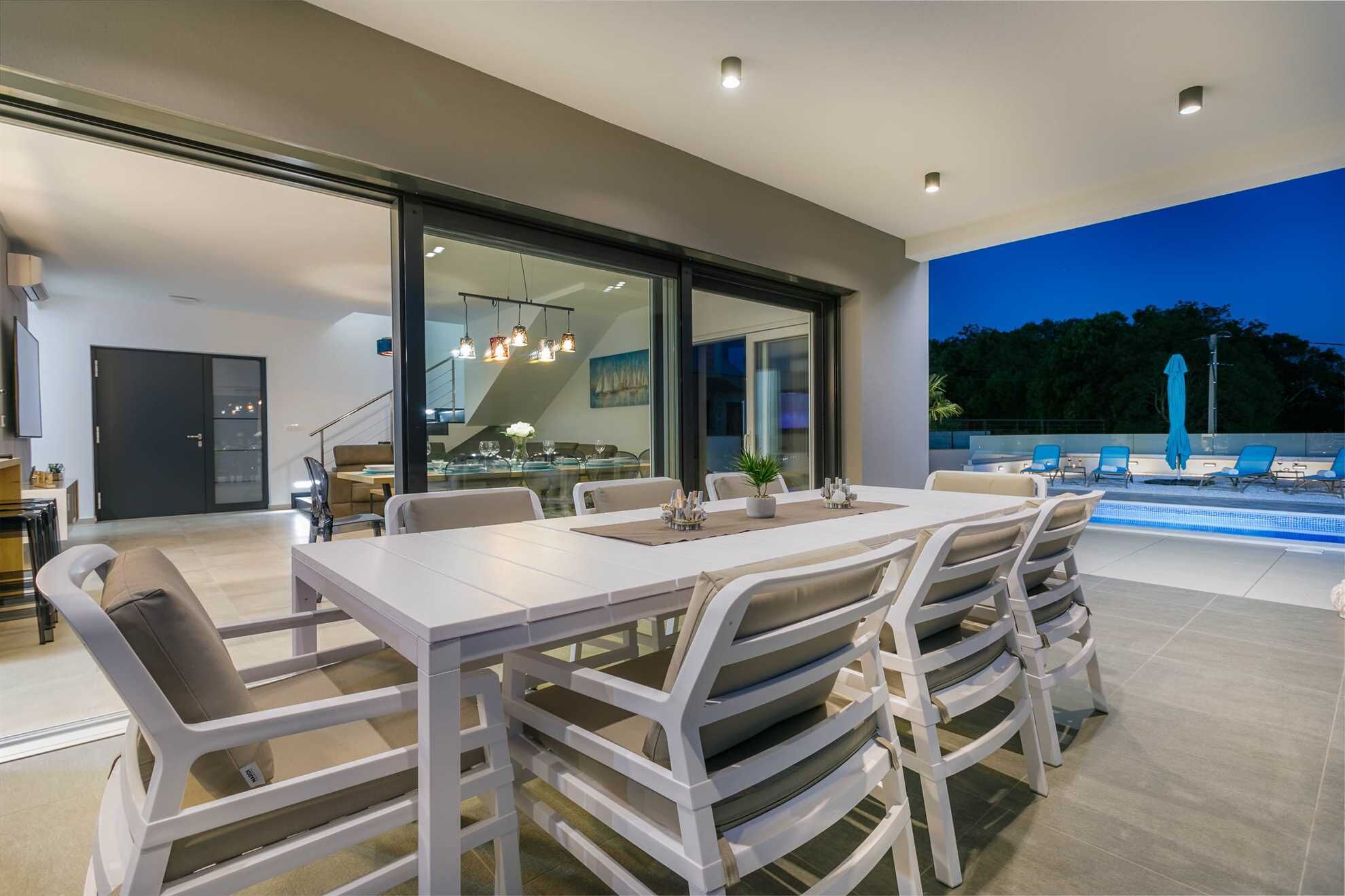 Un área de comedor exterior moderna con piscina y sillones de descanso.