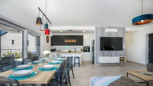 Une cuisine moderne dotée d’un grand téléviseur, un coin repas avec une table et des chaises en bois, et un canapé dans le salon.