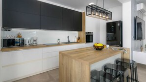 Une cuisine moderne avec des meubles de couleur sombre, un îlot central en bois et un luminaire suspendu.