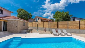 A swimming pool with a stone wall and a wooden fence in the background.