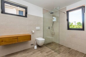 Une salle de bain moderne avec une douche à l’italienne en verre, un meuble-lavabo en bois et une fenêtre donnant sur un paysage verdoyant.
