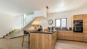 A modern kitchen with wooden cabinets, a central island, and a staircase leading to an upper level.
