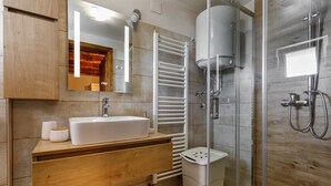 A modern bathroom with a wooden vanity, a white sink, a glass shower enclosure, and a towel rack. - Rustic apartment EVELIN close to the beach (Pinezići)
