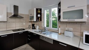 A modern kitchen with dark cabinets, a white countertop, a stove, a sink, and a microwave. - Rustic apartment EVELIN close to the beach (Pinezići)